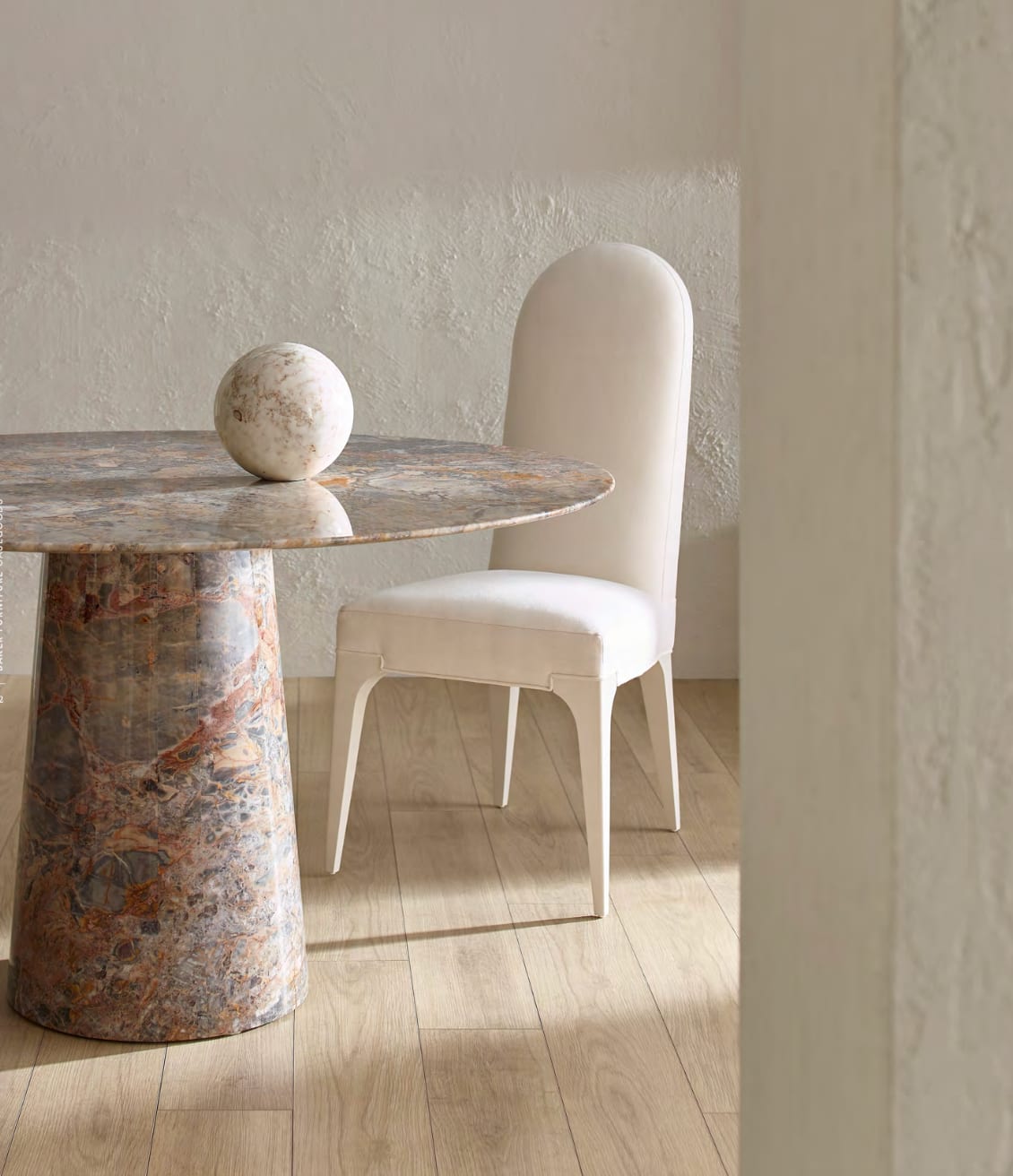 A breccia marble pedestal table and ivory linen chair on pale oak