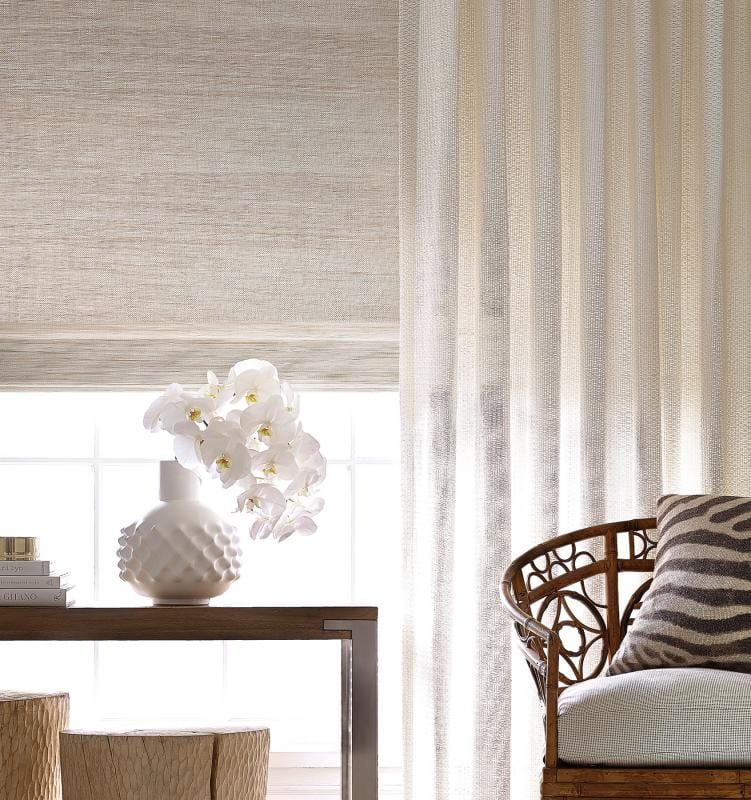A residential interior with a sheer drape and hand-loomed woven shade at the window, orchids on the sill