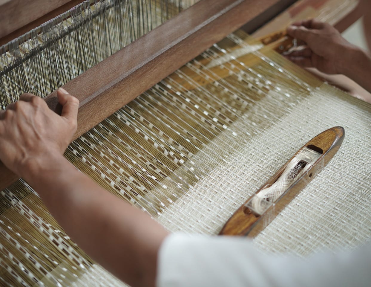 Hands at a traditional loom, weaving natural fibre by hand