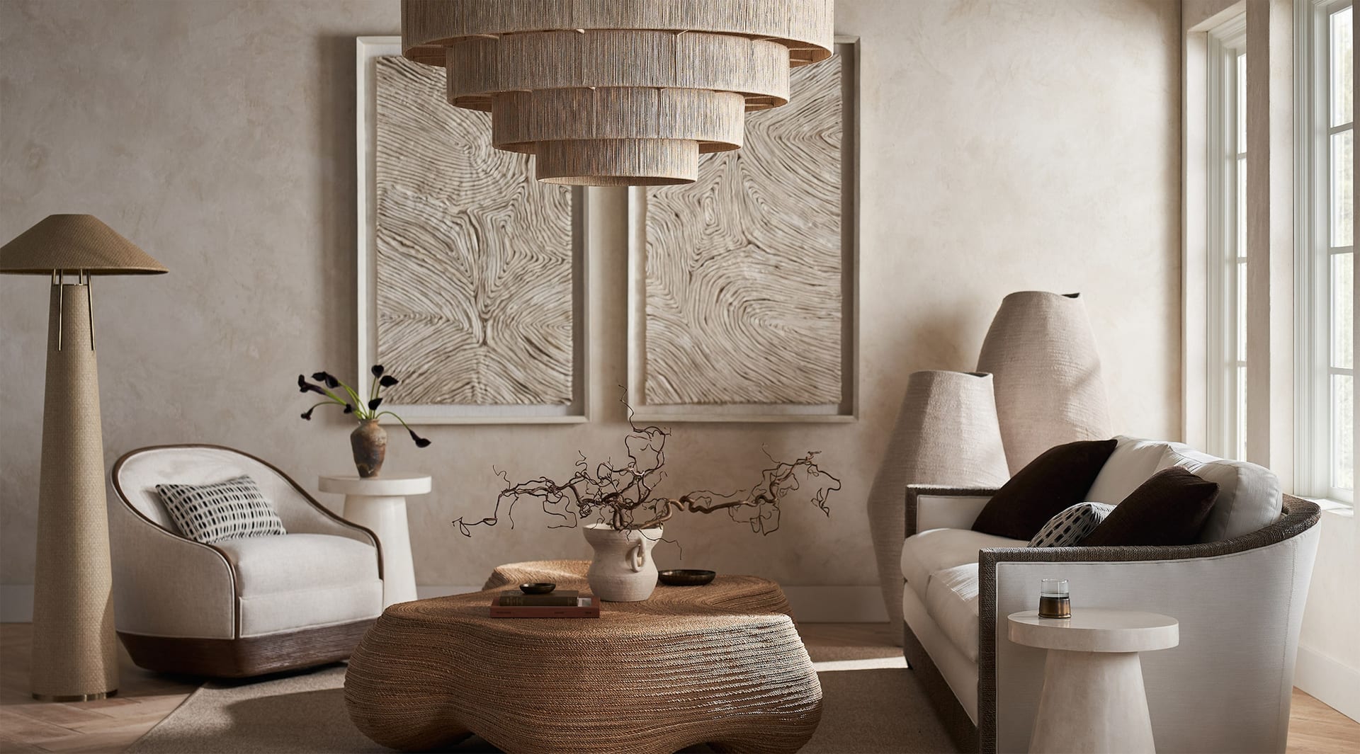 PALECEK — a plaster-walled living room held together by a sculptural rope chair, tiered raffia chandelier and woven coffee table