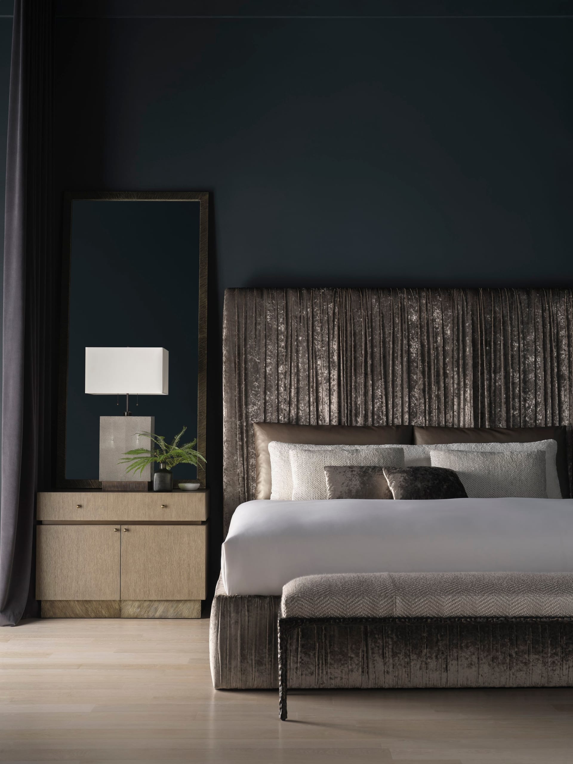 A bedroom set with the Fosser bed — sculpted upholstered headboard, dark walls, framed antique mirror