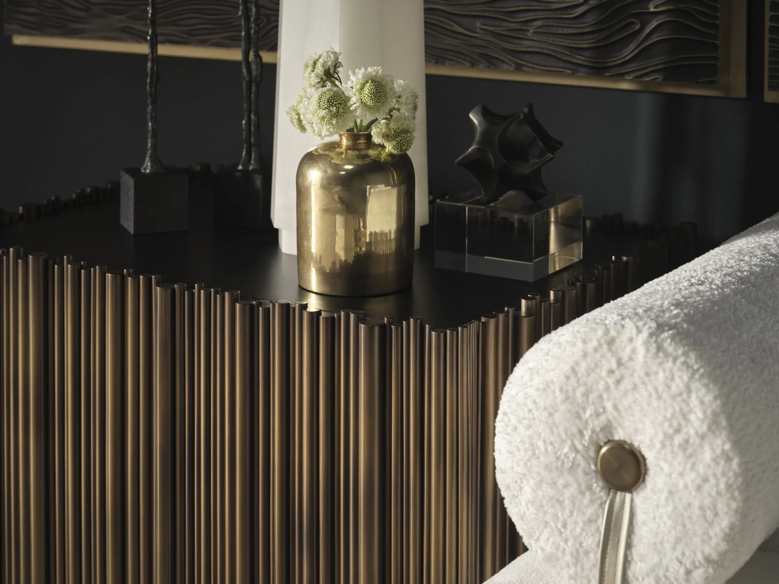 Detail of a textured bronze table base with honed stone top, gilt vase and cast sculpture