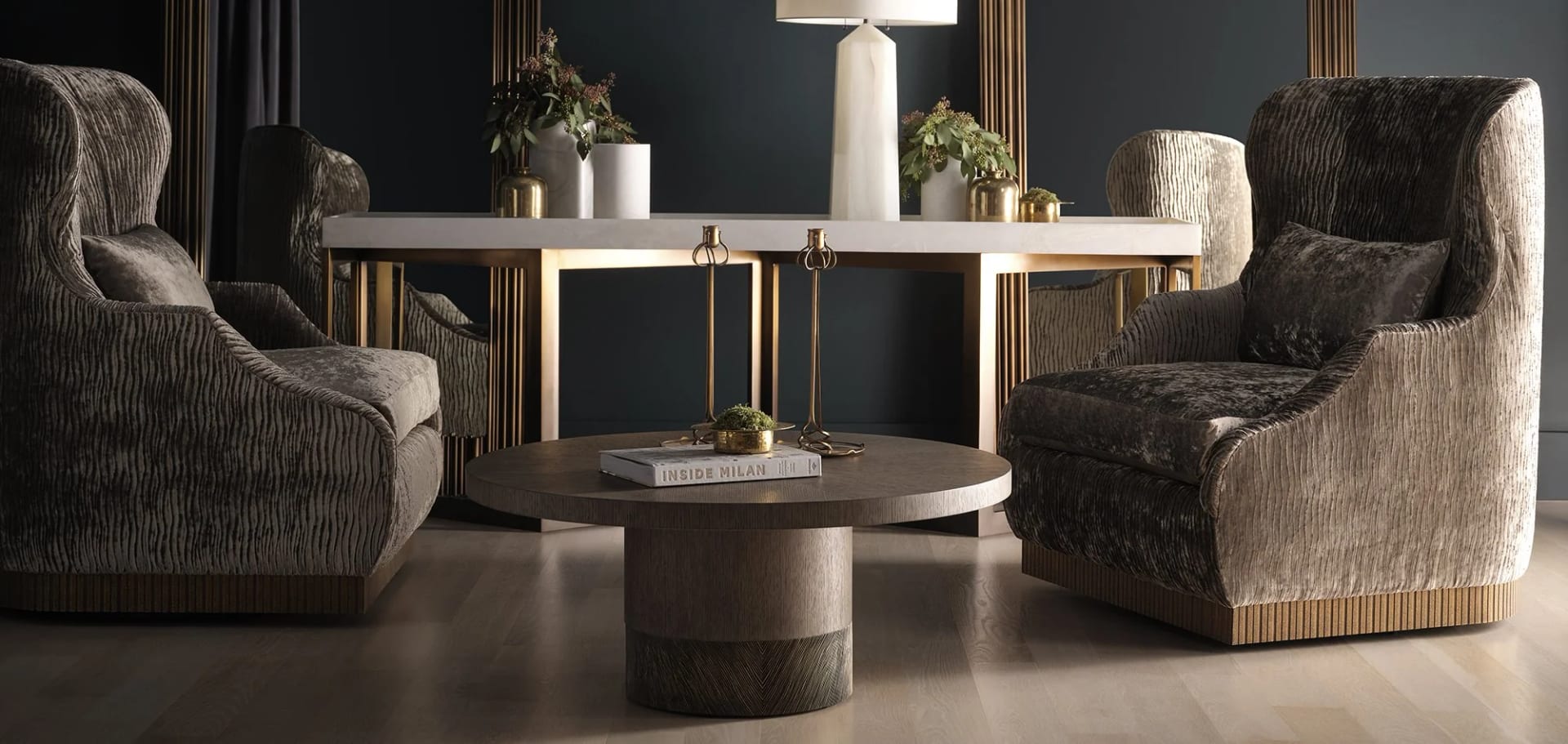 A layered living room — velvet armchairs, round bronze coffee table, books and a sculpted lamp