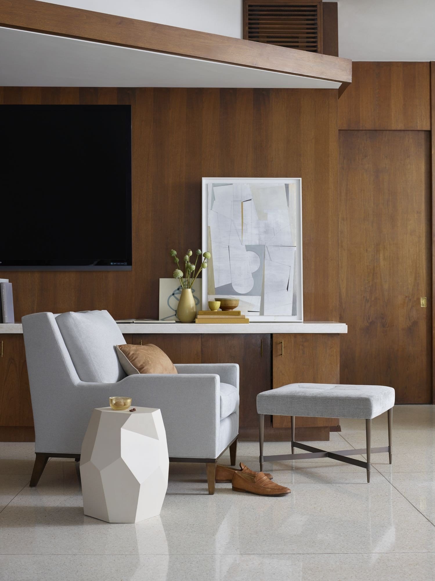 A pale grey armchair, geometric side table and footstool against a panelled wall